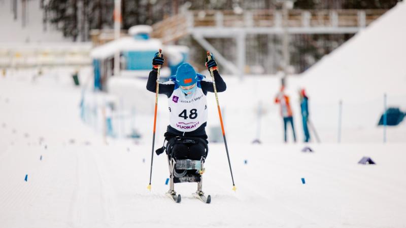 A sit skier competing in the cross-country competition pushing herself forward with two sticks