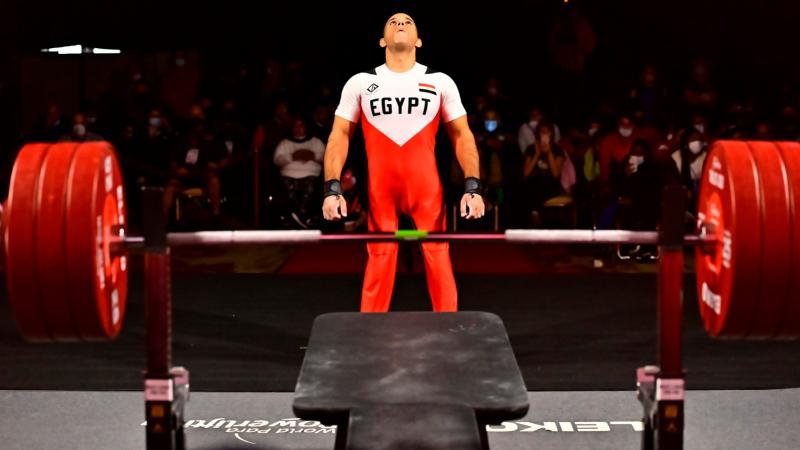 A man  looking up and standing in front of a bench press in a Para powerlifting