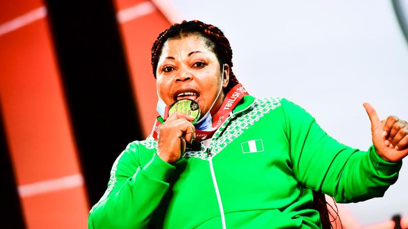 A woman in green uniform biting her gold medal