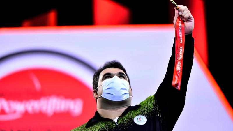 A man holding a gold medal and looking at the sky 