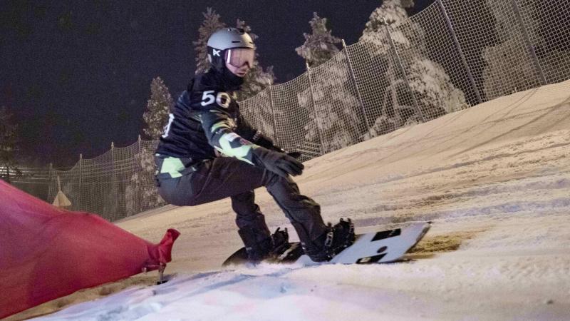 An athlete snowboarding during the night with goggles and helmet.