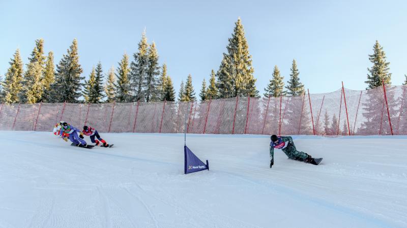 A male snowboarder ahead of three competitors in a snowboard cross