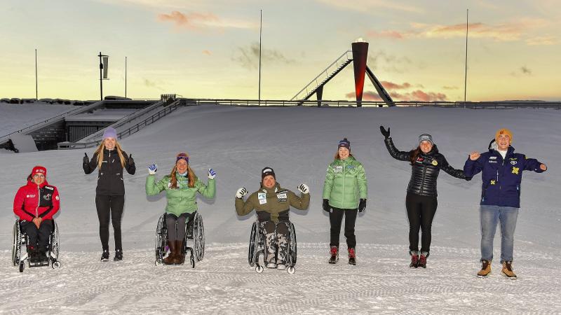 A group of three persons in wheelchairs and four standing persons on the snow