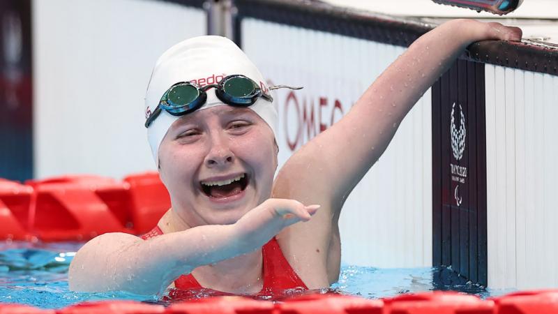 A Para swimmer hanging onto the edge of the pool with a smile on her face