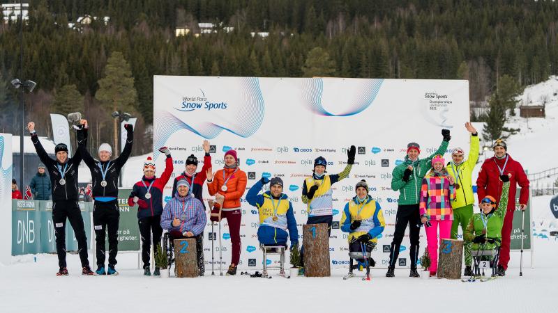 A group of 10 standing persons and four persons in wheelchairs in a medal ceremony on the snow