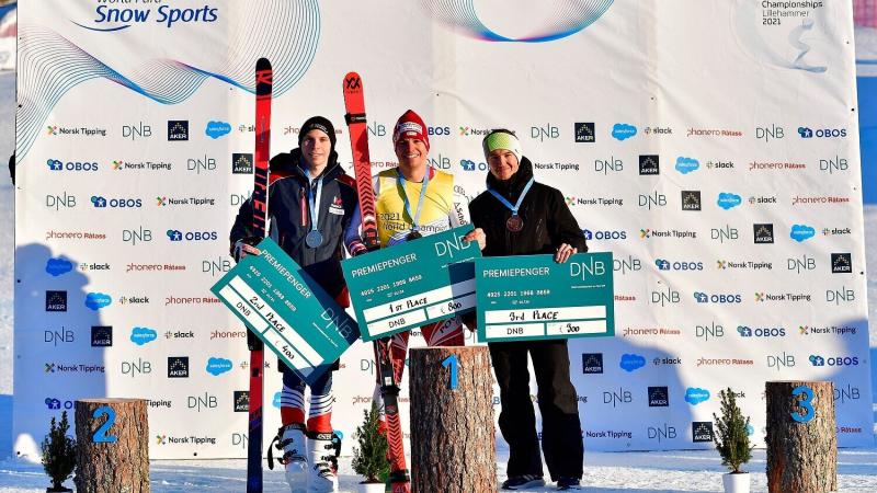 Three athletes standing in the snow in front of a white banner holding money prize.