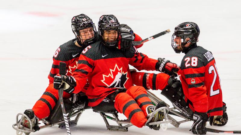 Three players in red and black jerseys smiling and hugging each other on the ice.