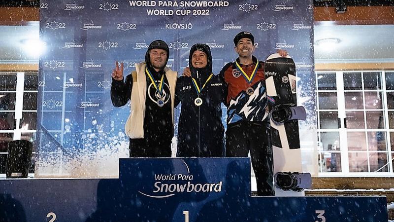 Three men with arms around each other on a snowboard podium