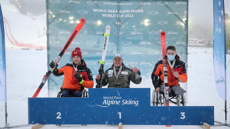 Three men in wheelchairs holding skis in a medal ceremony in the snow