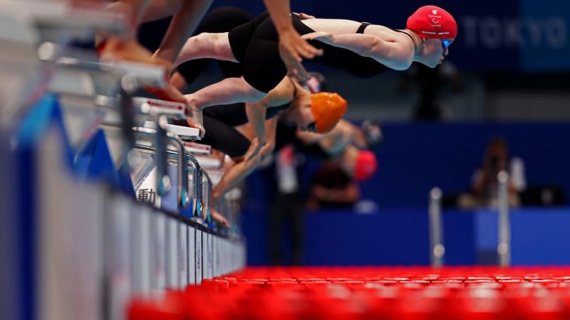 A female swimmers jumping from the starting block ahead of other competitors
