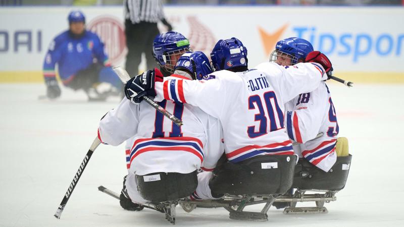 A group of Para ice hockey players on sledges celebrating the victory with a group hug.