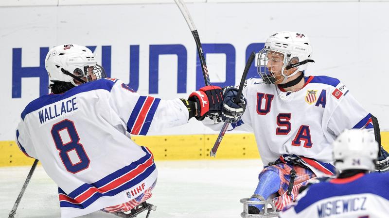 Two Para ice hockey players celebrating with a fist bump on their sledges.