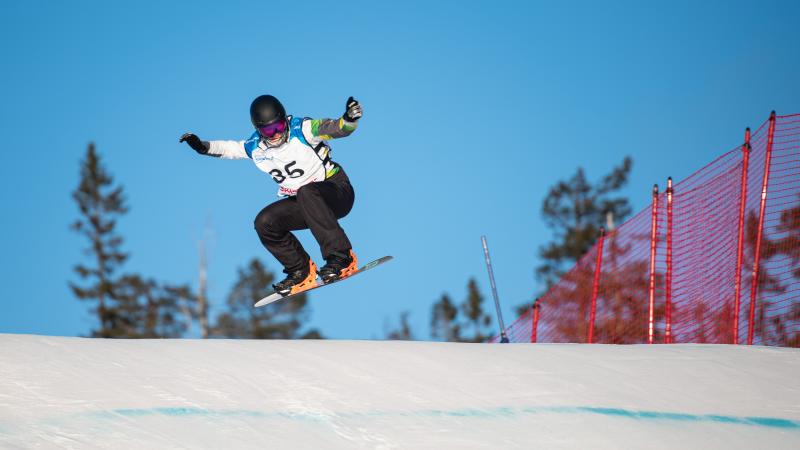 A man on a snowboard jumping into the air with his arms raised on a sunny day in the snow.