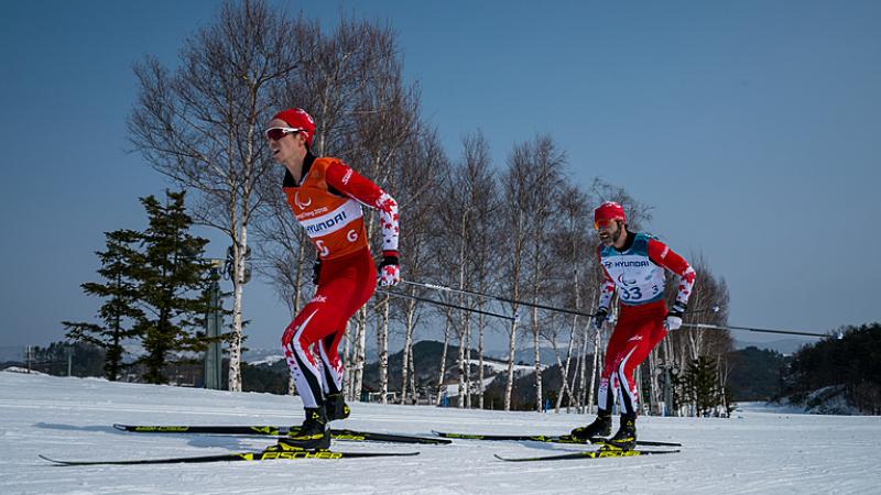 A male cross-country skier behind his male guide in a Para cross-country skiing race
