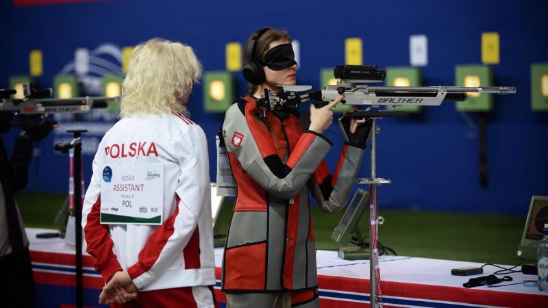 A vision impaired shooter blindfolded with her assistant behind her in a rifle competition