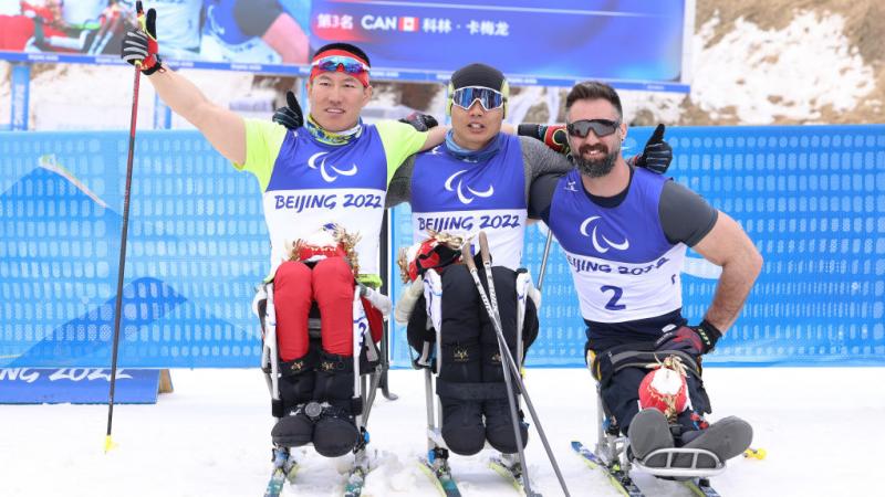 Gold medallist Zheng Peng of China (C), countrymate silver medallist Mao Zhongwu (L) and bronze medallist Collin Cameron of Canada (R) pose during Men's Sprint Sitting Final flower ceremony in the Beijing 2022 Paralympics Winter Games at Zhangjiakou National Biathlon Centre.