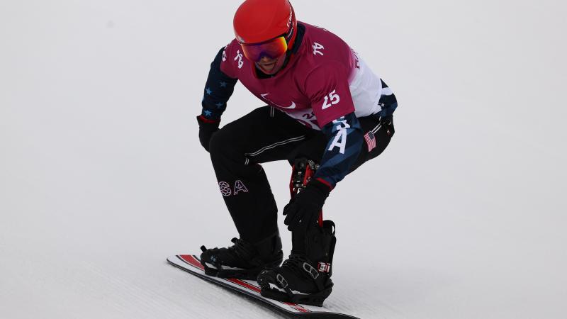 A man on a snowboard going down the snow with a helmet and goggles on his head.