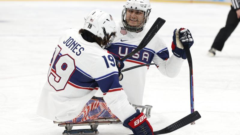 Two Para ice hockey players smiling to each other while on mono sleds.