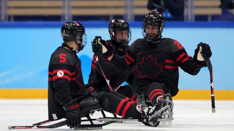 Three Para ice hockey players smiling to each other.