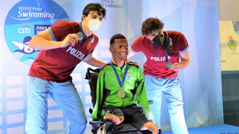 A man in a wheelchair in a medal ceremony with two standing men by his side