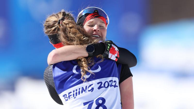 Emily Young and Natalie Wilkie of Canada embrace after winning gold in the Para Cross-Country Skiing Women's Long Distance Classical Technique Standing at Beijing 2022 Winter Paralympics. 