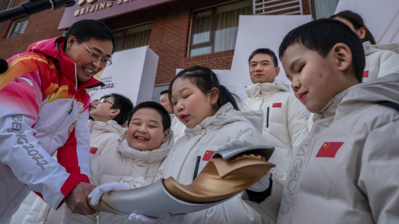 Students and choir members from the Beijing School for Blind feel and touch the torch as torchbearer Dr. Yao Yufeng (L) holds it out after the start of the Beijing 2022 Winter Paralympics Torch Relay. 
