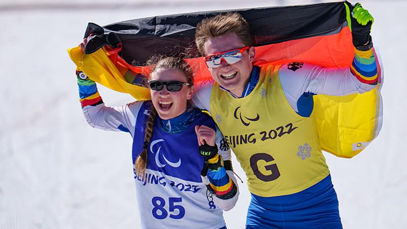 Leonie Maria Walter and Guide Pirmin Strecker hold the German flag behind them as they celebrate winning