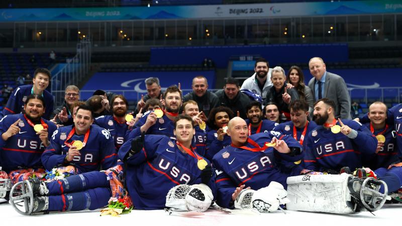Team USA Para ice hockey players in full gear without helmets posing for a photo with gold medals.