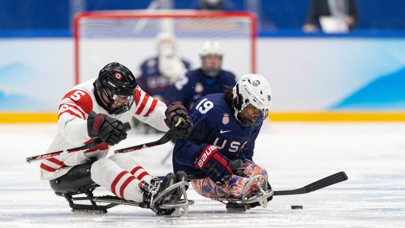 Two Para ice hockey players in full gear fighting for the possession.