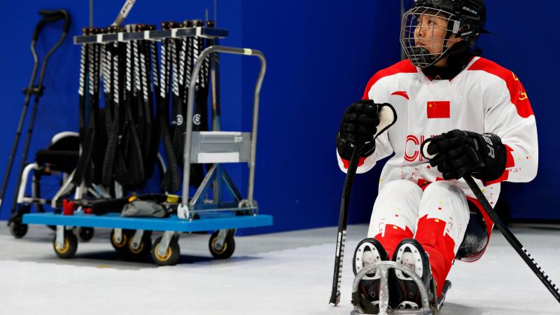 A woman sitting in a sled with a full Para ice hockey gear on her.