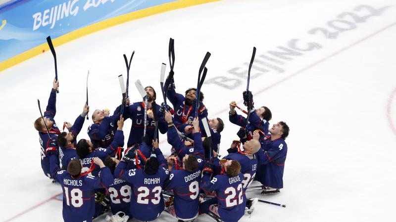 Team USA Para Ice Hockey players in full gear without helmets pointing with their sticks towards the top of the arena.