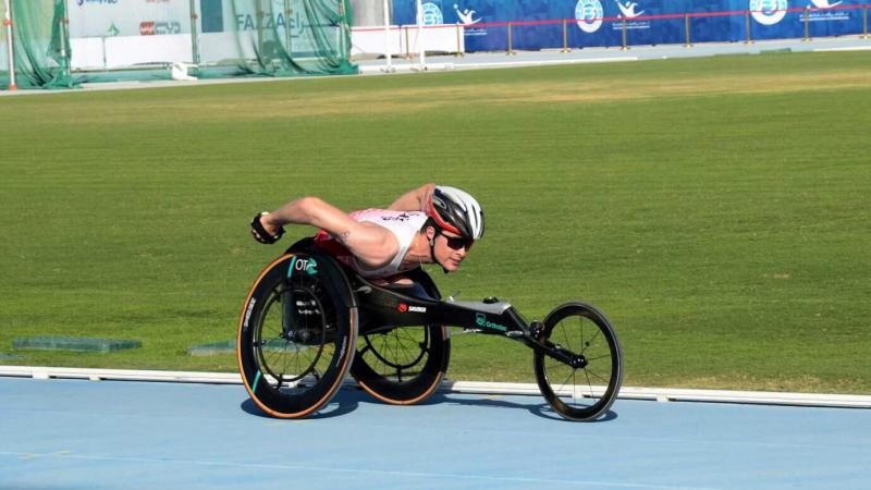 An athlete in a racing wheelchair pushing himself forward with both hands.