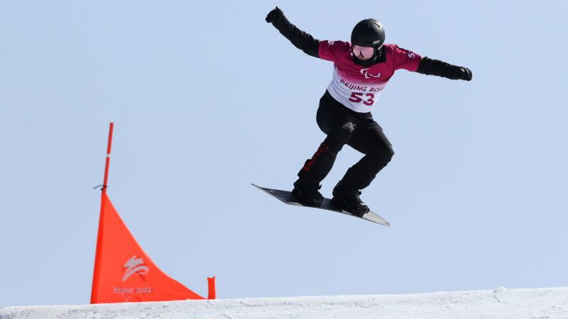 A man passing by a flag in a Para snowboard competition 