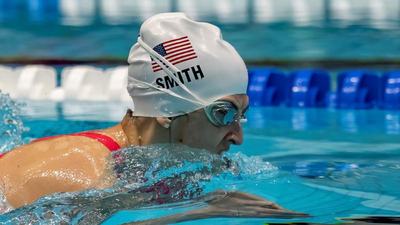 A female Para swimmer with a white cap swimming breastroke