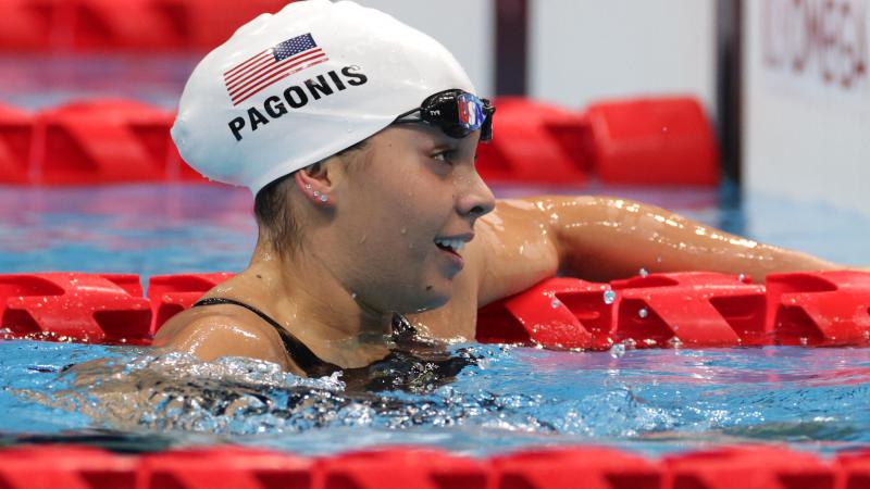 A female Para swimmer hanging on a rope with her left hand and the goggles off.