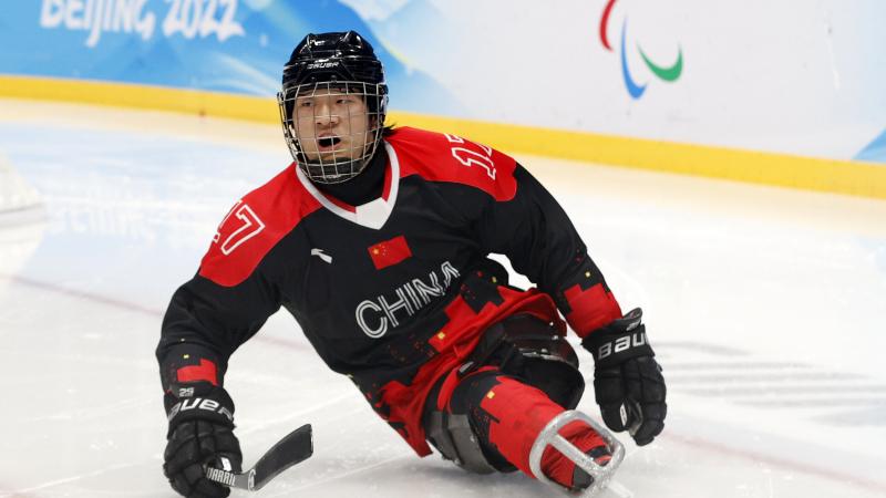 A Para ice hockey player in full gear slides on the ice.