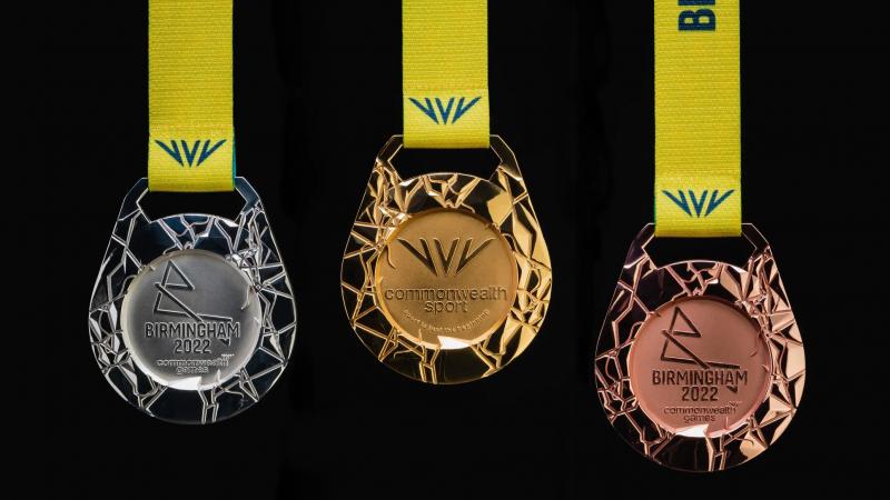 Three medals, gold, silver and bronze, are featured on a black background, each medal having a unique embossed design that symbolises an aerial map of the host region's road and canal network. 