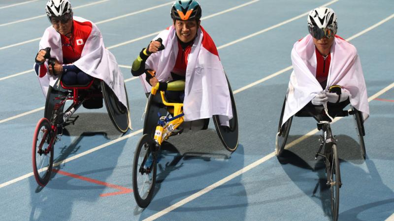 Three men in racing wheelchairs on an athletics track