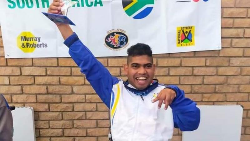 Liakath Aziz raises his arm in celebration while holding a trophy.