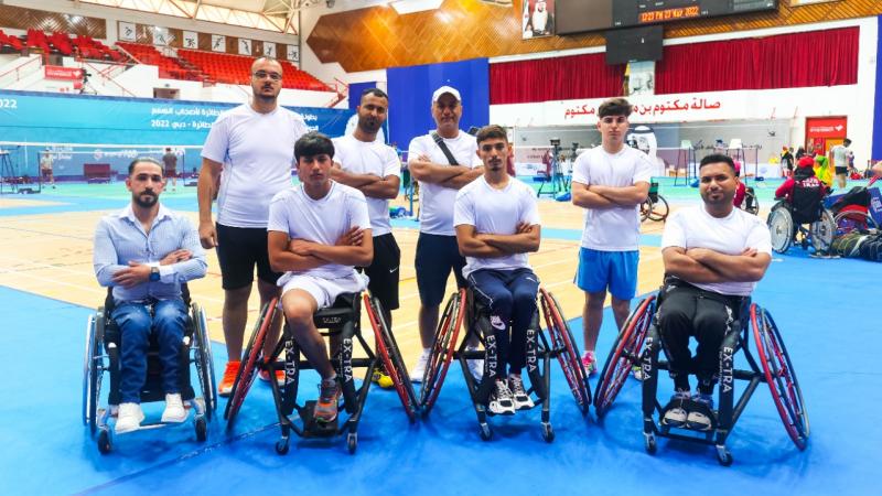 Eight athletes and staff of the Iraqi Para badminton team pose for a photo near the court.