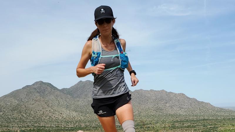 Jacky Hunt-Broersma runs along a sandy trail in Arizona with a mountain backdrop.