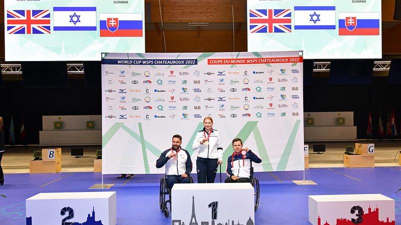 A woman standing on a podium between two men in wheelchairs