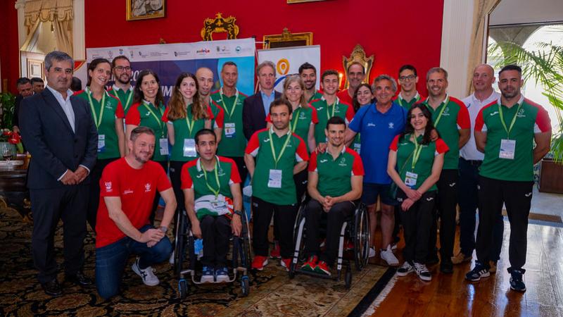 A group of people wearing the uniform of the Portuguese Para swimming team posing for a picture in a hall