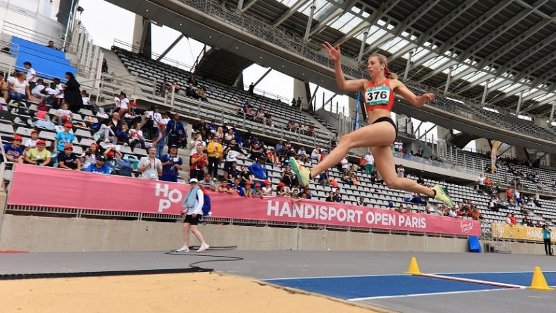 A woman competing in the long jump in front of the spectators in a stadium