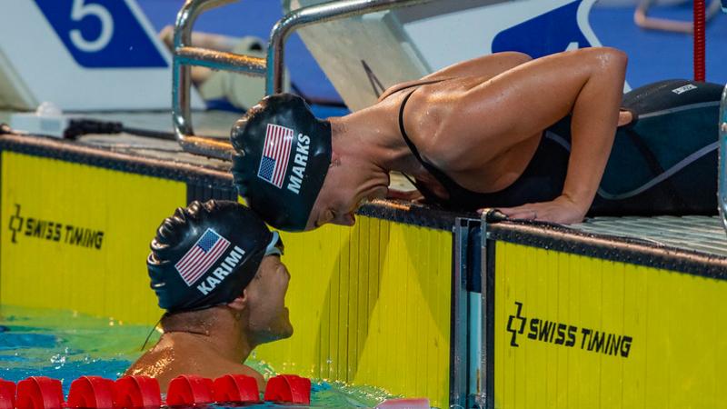 A woman outside a swimming pool stretching her head to touch the head of a man inside the pool