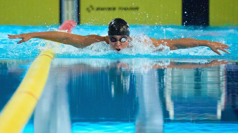 A female swimmer in a black cap swimming butterfly