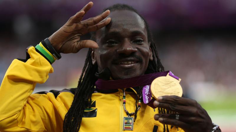 Jamaica's Alphanso Cunningham holds up his gold medal in the men's javelin throw F52/53 and waves with his other hand while posing for photos on the London 2012 podium.