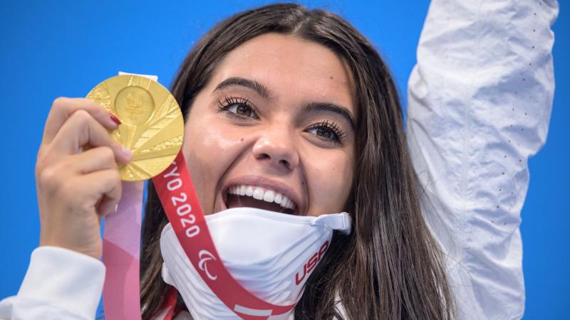 Anastasia Pagonis smiles widely as she holds up her gold medal and raises her other arm in celebration at Tokyo 2020.