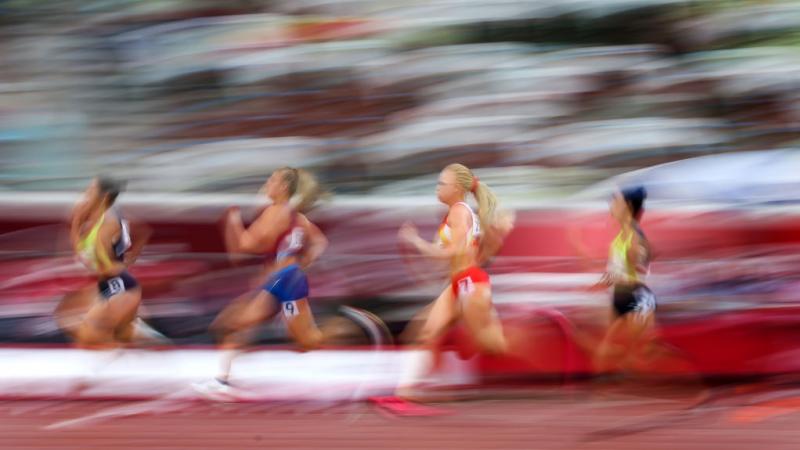 A blurred image of four women competing in an athletics track
