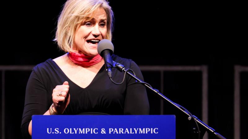 A woman makes a speech at a tribune marked with the words 'U.S. Olympic and Paralympic Hall of Fame'.